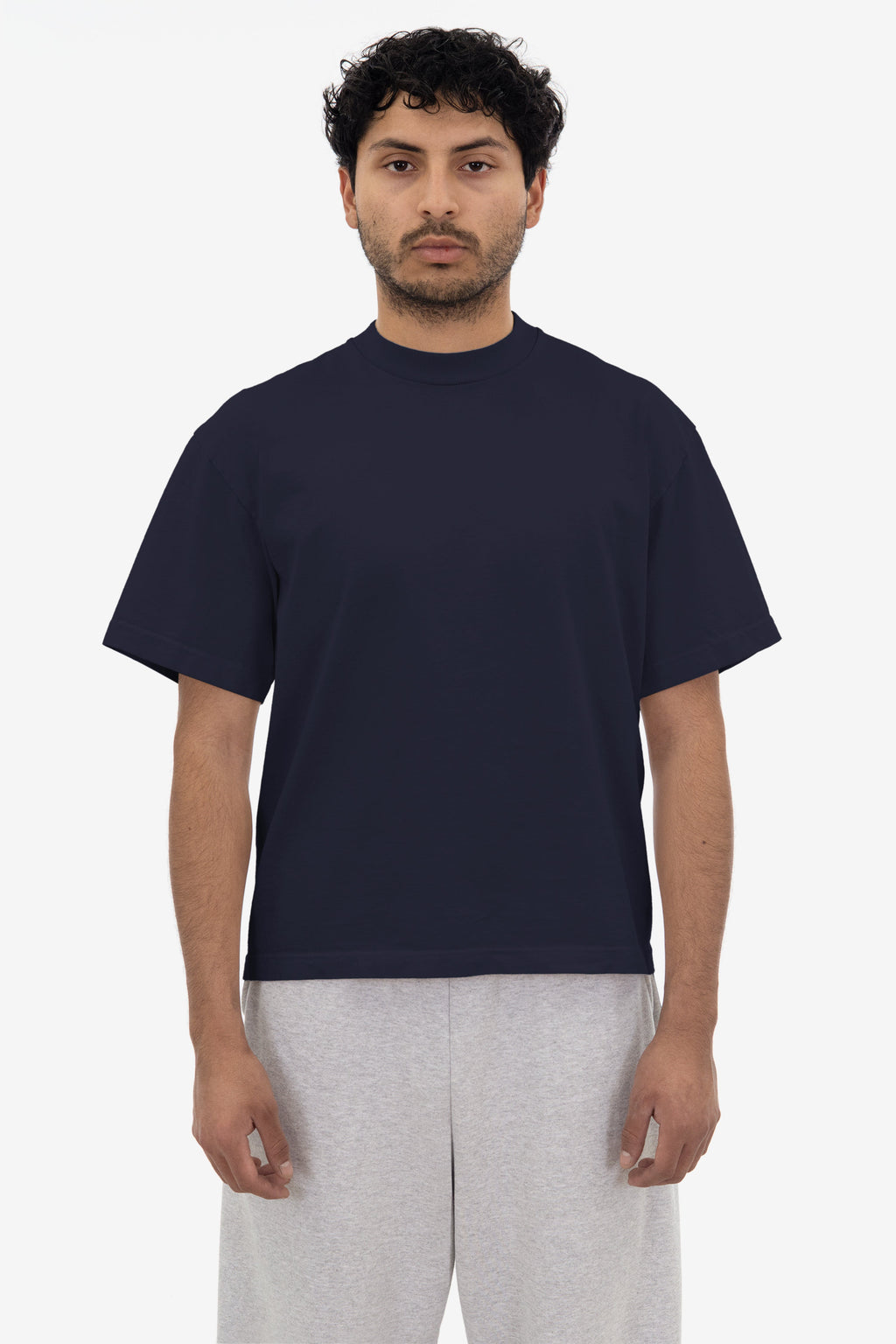 Man wearing a navy blue t-shirt and light gray pants on a white background