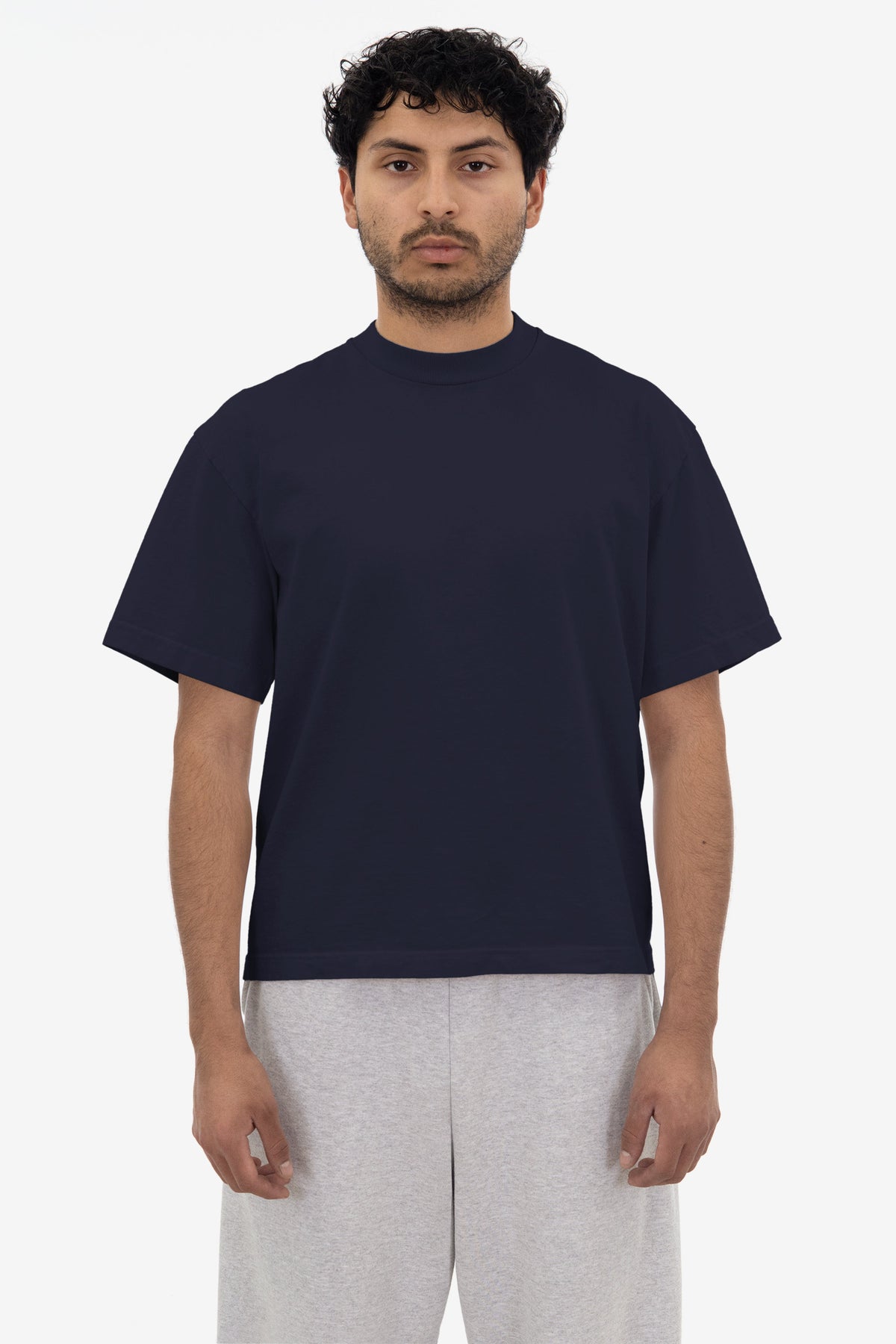 Man wearing a navy blue t-shirt and light gray pants on a white background